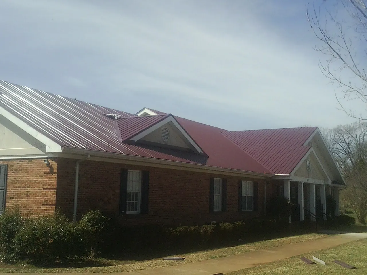 Red metal roof with gabled entries on a long brick building, from a Hail Damage Roof Repair job in Mendon
